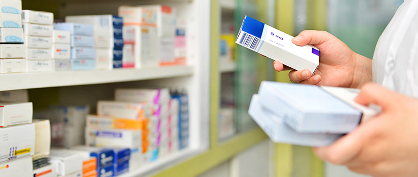 pharmacist holding boxes of medicine in front of a wall of medications
