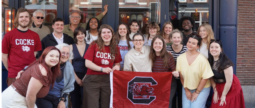 A group of USC students gather for a group photo with USC shirts and flag.