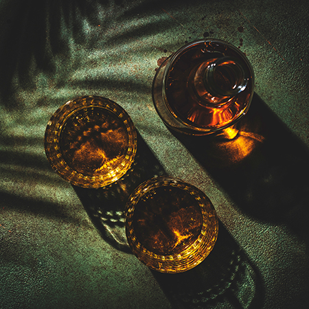 Whiskey, scotch or bourbon in glasses and bottle, green stone background with hard light, shadows and sun glare, copy space