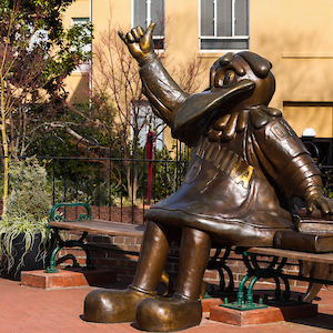 bronze statue of cocky sitting on a bench photographed from the side