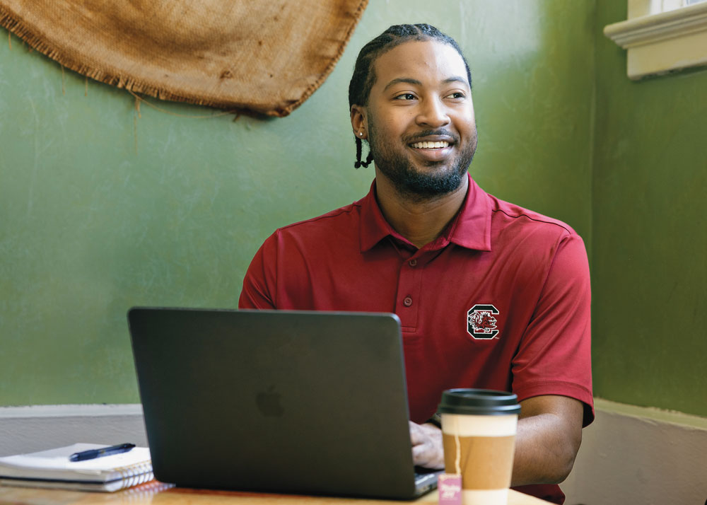 Jakhi Brown sits with his computer and a cup of tea.